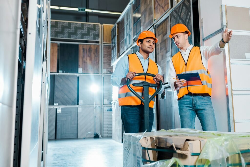 warehouse worker pointing with hand near indian colleague with pallet jack